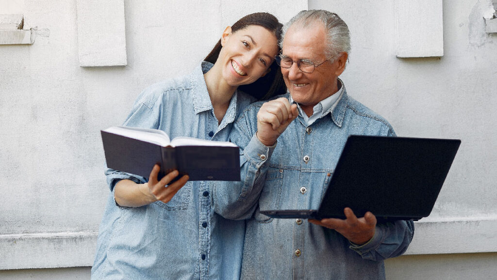 Padre e figlia. Lei tiene un libro mentre lui un computer portatile